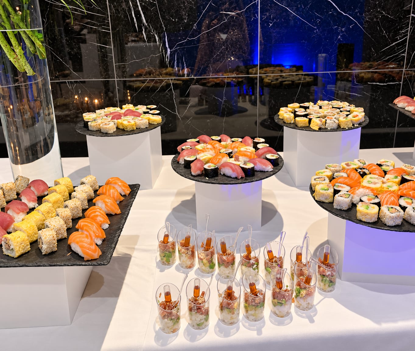 Plateaux de sushis et de makis sur socles blancs, devant des verrines de riz tartare