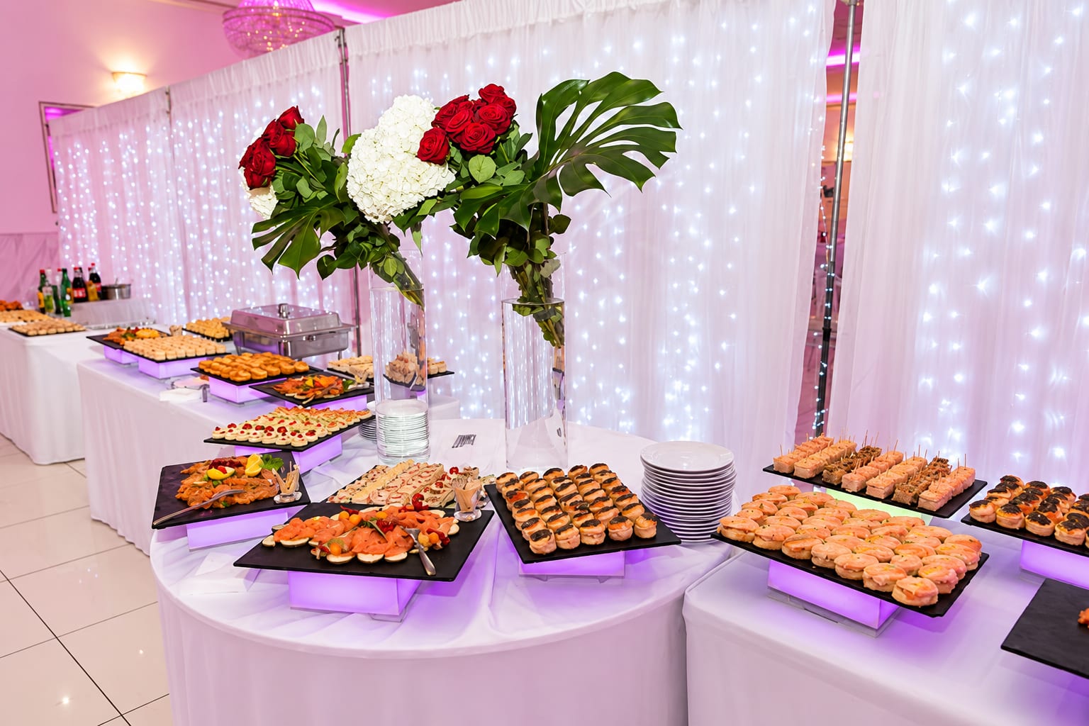 Buffet de cocktail sur ardoises lumineuses, sous des bouquets de roses rouges et d'hortensias blancs