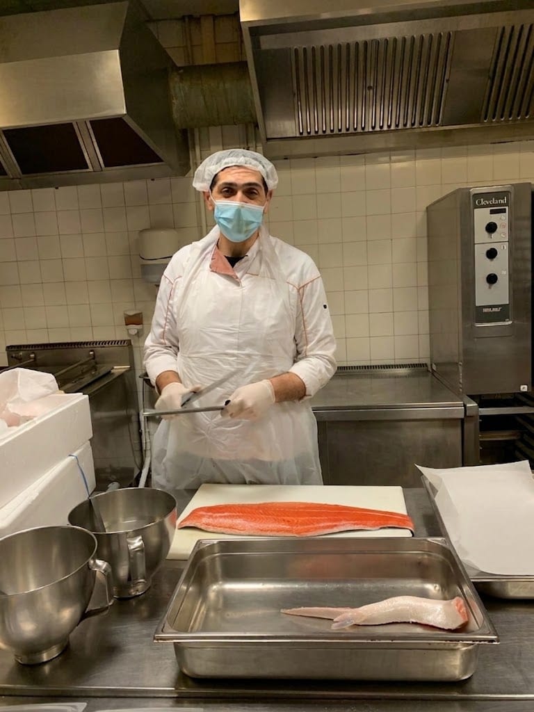Cuisinier en tenue, filet de saumon sur la planche, en cuisine centrale